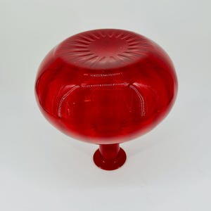 May include: A vibrant red glass vase with a round, bulbous top and a short, pedestal base. The vase has a glossy finish, reflecting light and creating a striking visual effect. The design is simple yet elegant.
