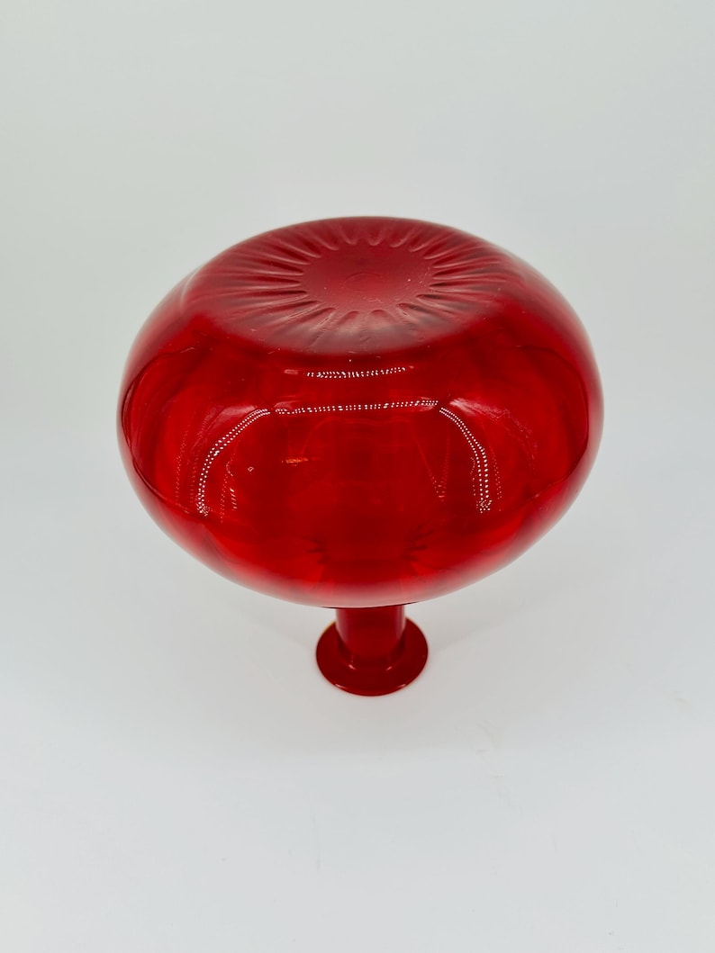 May include: A vibrant red glass vase with a round, bulbous top and a short, pedestal base. The vase has a glossy finish, reflecting light and creating a striking visual effect. The design is simple yet elegant.