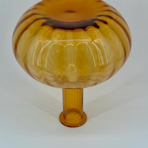 May include: A decorative amber-colored glass bowl with a rounded top and a short, cylindrical stem. The bowl has a striped pattern in shades of amber and brown. The stem has a circular base. The glass bowl is likely for decorative purposes.