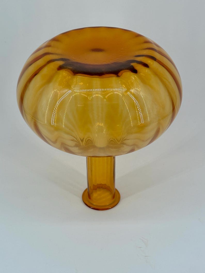 May include: A decorative amber-colored glass bowl with a rounded top and a short, cylindrical stem. The bowl has a striped pattern in shades of amber and brown. The stem has a circular base. The glass bowl is likely for decorative purposes.