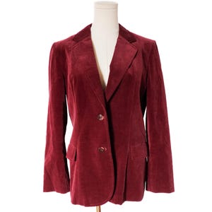 May include: A burgundy velvet blazer with a notched lapel and two-button closure. The blazer has two front pockets and is displayed on a mannequin. The fabric has a soft, textured appearance.