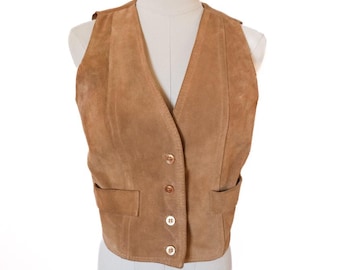 May include: A tan suede vest with a V-neck and four button closure. The vest has two front pockets and is displayed on a mannequin. The vest is a neutral color and could be worn with many different outfits.