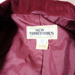 May include: Close-up of a burgundy velvet jacket interior. The lining is a matching shade of burgundy. A tag reads "NEW TERRITORIES" and "MADE IN JAPAN". The tag also indicates a size 13. Dry clean only.