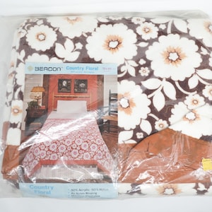 May include: A Beacon Country Floral blanket in a clear plastic package. The blanket features a brown background with large white and tan floral patterns. The packaging includes the text "Country Floral" and "50% Acrylic 50% Nylon". The blanket measures 72 x 90 inches.