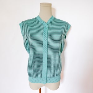 May include: A sleeveless, button-down top displayed on a mannequin. The top features horizontal black and light blue stripes across the body. The button placket and trim have a light blue polka dot pattern. The top is made of a knit fabric.