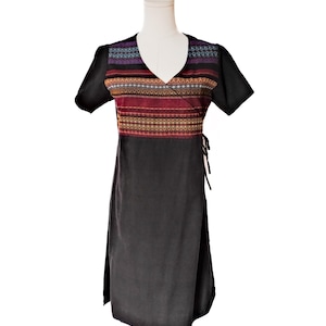 May include: Black wrap dress with short sleeves and a V-neck. The bodice features a colorful, patterned fabric in shades of red, orange, purple, and gold. The dress has a tie closure at the waist and is displayed on a mannequin.