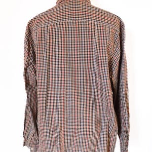 May include: A long-sleeved button-down shirt displayed on a mannequin. The shirt features a classic plaid pattern in red, black, blue, and tan. The collar and buttoned cuffs are visible. The shirt is made of a woven fabric.