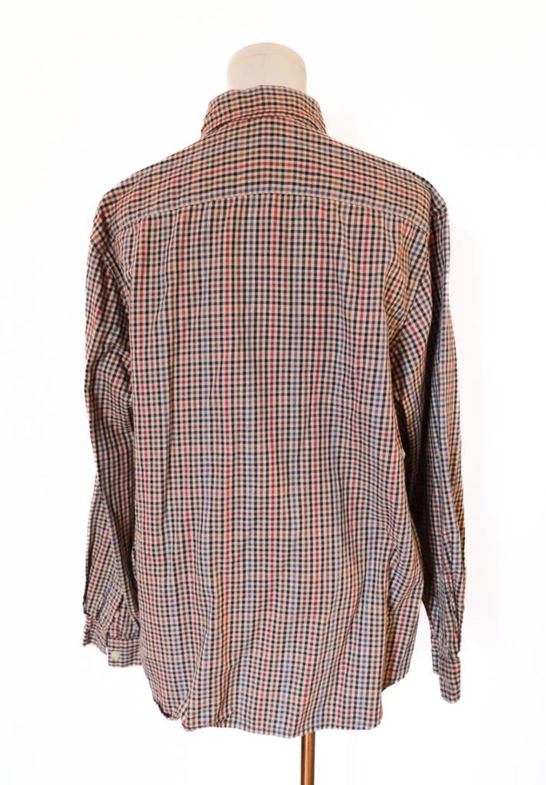 May include: A long-sleeved button-down shirt displayed on a mannequin. The shirt features a classic plaid pattern in red, black, blue, and tan. The collar and buttoned cuffs are visible. The shirt is made of a woven fabric.