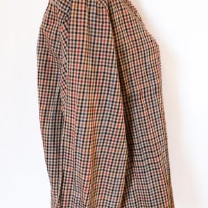 May include: A long-sleeved button-down shirt with a classic plaid pattern in shades of brown, red, black, and blue. The shirt is displayed on a mannequin, showcasing the collar and sleeve details. The fabric appears to be a woven material.
