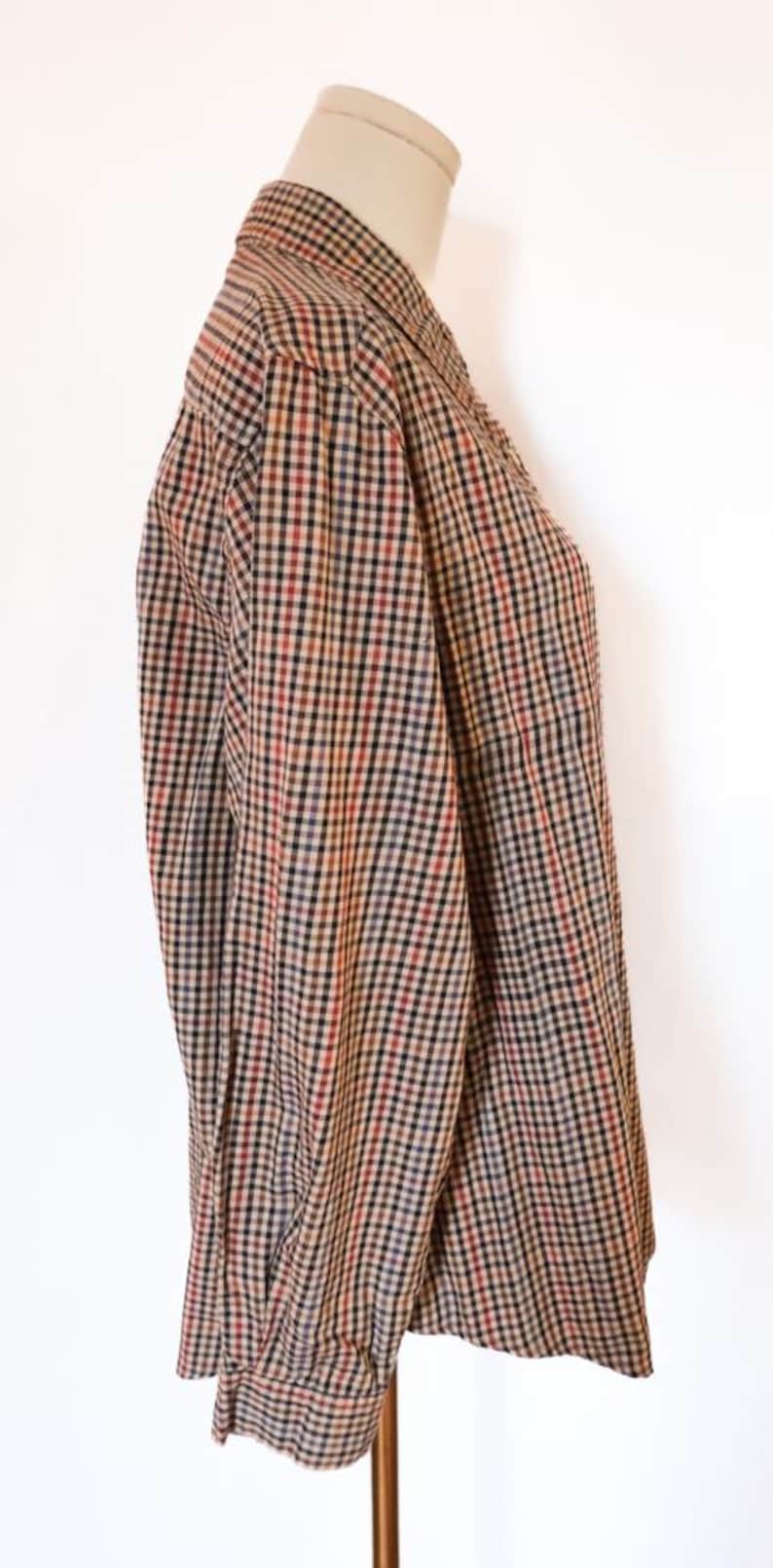 May include: A long-sleeved button-down shirt with a classic plaid pattern in shades of brown, red, black, and blue. The shirt is displayed on a mannequin, showcasing the collar and sleeve details. The fabric appears to be a woven material.
