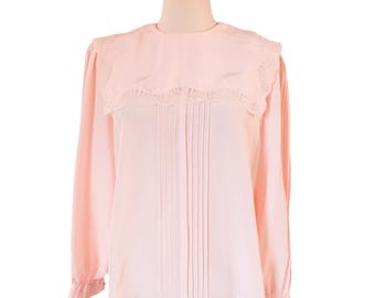 May include: A light pink long-sleeve blouse featuring a wide, rounded collar with intricate lace trim detailing. The front of the garment displays vertical pleats running down the center, complemented by long sleeves with cuffs.