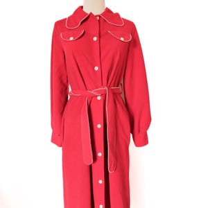 May include: A bright red dress with a collared neckline, button-down front, and long sleeves. The dress features white scalloped trim on the collar, pockets, and cuffs. A matching belt cinches the waist. The dress is displayed on a mannequin.