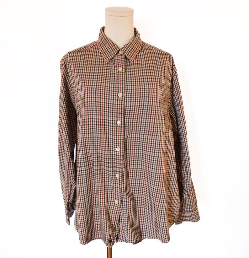 May include: A button-down shirt with a classic plaid pattern in shades of brown, red, black, and white. The long-sleeved shirt is displayed on a mannequin, showcasing its collar and buttoned front. The shirt is made of a lightweight fabric.