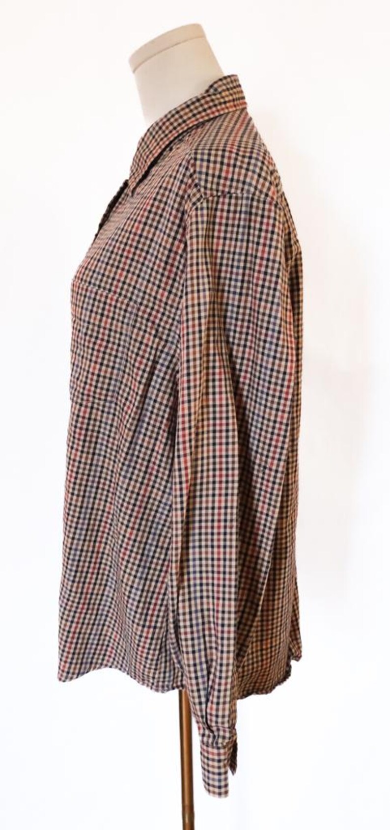 May include: A button-down shirt with a classic plaid pattern in shades of brown, black, red, and blue. The long-sleeved shirt is displayed on a mannequin, showcasing the collar, buttoned cuffs, and a chest pocket.