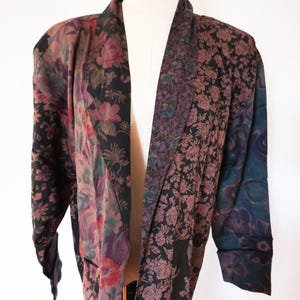 May include: A patchwork floral print jacket in shades of black, purple, and burgundy. The jacket features a shawl collar and long sleeves. The floral patterns include roses and other flowers. The jacket is displayed on a mannequin.
