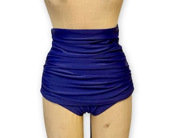 May include: A navy blue high-waisted swimsuit bottom with a ruched design. The garment is displayed on a mannequin. The fabric has a smooth, solid appearance. The style is reminiscent of vintage swimwear.