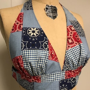 May include: A patchwork halter top in red, white, and blue. The top features a mix of patterns, including gingham, paisley, and floral designs. The top is displayed on a mannequin.