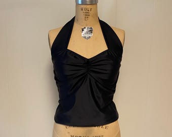 May include: A solid black halter top featuring a sweetheart neckline with a gathered, ruched center detail. The sleeveless garment is displayed on a beige dress form mannequin that has the text WOLF MODEL 1977 printed on the front surface.