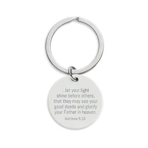 May include: A silver-colored keychain with a circular pendant. The pendant has the text "...let your light shine before others, that they may see your good deeds and glorify your Father in heaven. Matthew 5:16" in gray.