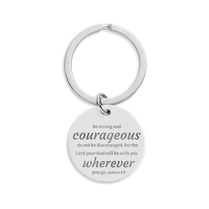 May include: A silver-colored keychain with a round pendant. The pendant has the words "Be strong and courageous" and a Bible verse printed in gray. The keychain is a religious-themed accessory.