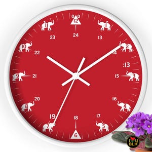 May include: A round wall clock with a white frame and a red face. White elephant silhouettes mark the hours. The clock hands are white. A small potted plant with purple flowers is in the lower right corner.