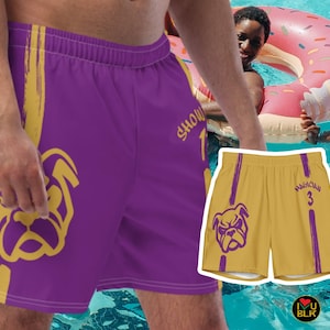 May include: Purple swim trunks with a gold bulldog graphic and vertical stripes. The trunks have the word "SHOW" and the number "1" printed on them. A smaller pair of gold swim trunks with a bulldog graphic is also visible.