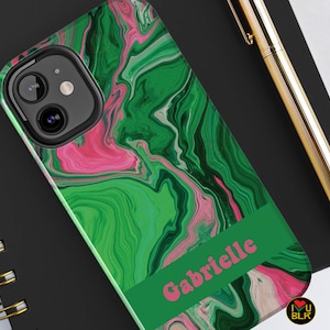 May include: A green and pink marbled phone case with a black camera lens and the name "Gabrielle" printed in pink letters.
