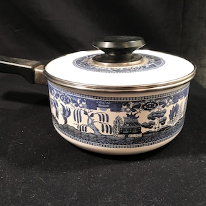 May include: A white and blue patterned saucepan with a black handle and lid. The blue pattern depicts a landscape scene. The saucepan is made of metal and has a silver rim.