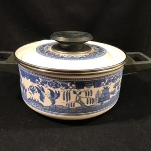 May include: A white and blue ceramic pot with a lid. The pot features a blue and white Willow pattern design around the exterior. The lid has a black handle. The pot has two gray handles on either side.