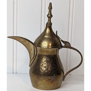 May include: A brass teapot with an ornate floral design. The teapot has a spout, a handle, and a lid with a finial.