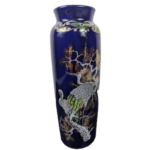 May include: A tall, navy blue ceramic vase with a detailed crane and tree design. The vase features gold accents around the rim and on the branches, with green and white details on the birds and foliage. The vase is approximately 12 inches tall.