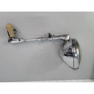 May include: Vintage chrome car headlight with a cream-colored handle. The headlight has a round, reflective lens and a long, adjustable arm. The item is likely from the early to mid-20th century.