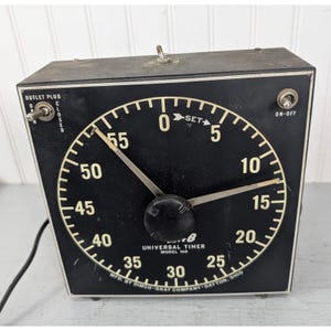 May include: A black Dimco-Gray Universal Timer Model 168 with a large circular face, white numerical markings from 0 to 55, two metal hands, a central black knob, and toggle switches labeled Outlet Plug and On-Off, manufactured in Dayton, Ohio.