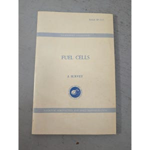 May include: A cream-colored softcover book titled Fuel Cells: A Survey, published by the National Aeronautics and Space Administration. The cover features blue text, two horizontal blue stripes, and the circular NASA logo at the bottom center.