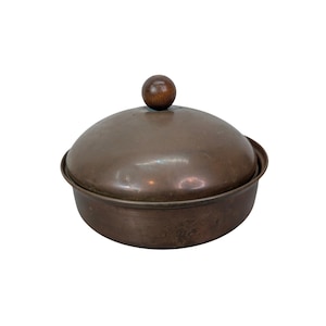 May include: A copper-colored, lidded serving dish with a wooden knob on top. The dish has a rounded shape and a slightly textured surface. The lid fits snugly over the base, creating a complete and functional piece.