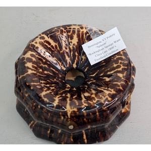 May include: A brown and tan Rockingham Sponge Ware spitoon from Bennington, VT Pottery, circa late 1800s. The ceramic piece has a unique pattern and is in excellent condition. The spitoon has a circular opening in the center.