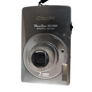May include: A silver Canon PowerShot SD750 digital camera. The camera has a zoom lens and a 7.1 megapixel resolution. The Canon logo and model information are printed on the front of the camera.