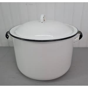 May include: A white enamel pot with a lid. The pot has a black rim and handles. The lid has a small handle. The pot is sitting on a gray surface.