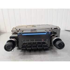 May include: A vintage Delco car radio featuring a black rectangular faceplate with a horizontal frequency dial ranging from 5 to 16. The unit includes five black push buttons, two large black control knobs with chrome trim, and a metal casing.