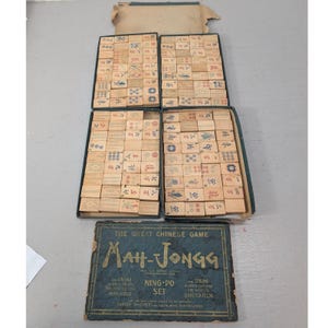 May include: A vintage Mah-Jongg game set by Parker Brothers, featuring four rectangular trays filled with wooden tiles marked with Chinese characters and symbols in blue and red ink, alongside a dark blue box lid with gold text.
