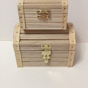 May include: Two wooden treasure chests with gold-colored hinges and decorative accents. The smaller chest is stacked on top of the larger chest.
