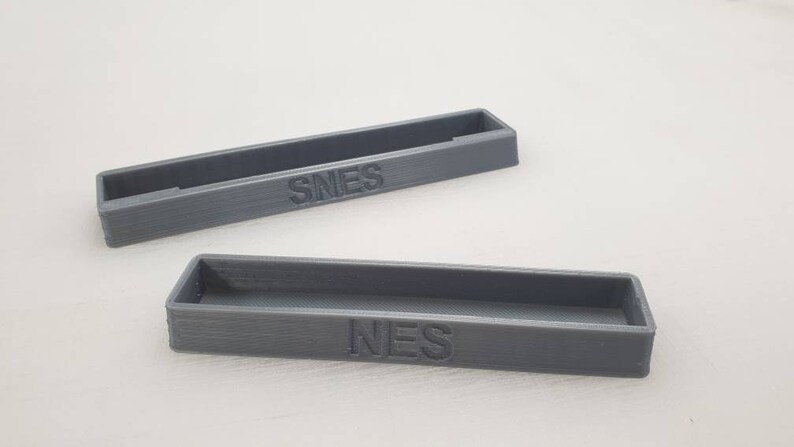 May include: Two gray plastic storage containers with the words "NES" and "SNES" printed on them.