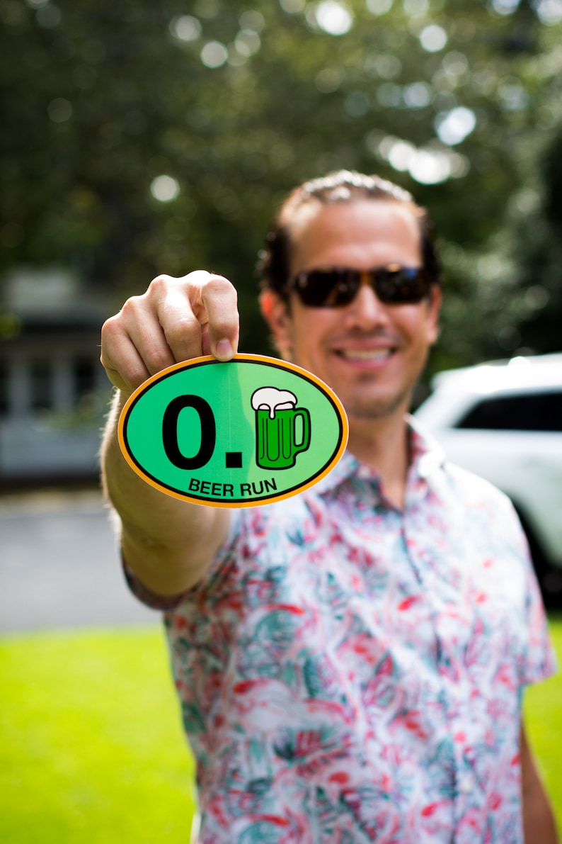 May include: A person holding a green and yellow round sticker with the text "0. BEER RUN" and a green cartoon beer mug.