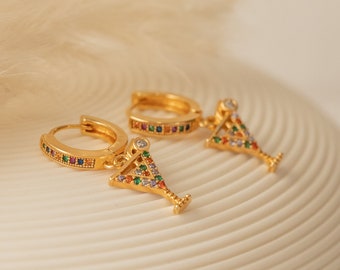Puede incluir: Un par de pendientes de aro dorados con un colgante de copa de martini. La copa está decorada con piedras preciosas de colores.