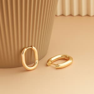 May include: Two gold oval hoop earrings on a light brown surface. The earrings are simple and elegant.