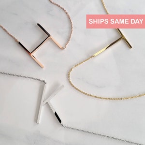 Puede incluir: Tres collares iniciales en oro rosa, oro y plata. Las letras H, T y K se muestran en delicadas cadenas. Los collares están sobre una superficie de mármol blanco. El texto "SHIPS SAME DAY" está en un rectángulo rosa.