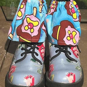 May include: A pair of blue floral print boots with black laces and a black rubber sole. The boots have a blue and white fabric covering the top of the boot with a pink and brown ice cream cone pattern.