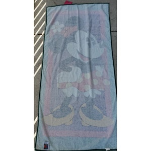 Pu&ograve; includere: Un asciugamano da spiaggia bianco con un'immagine colorata di Minnie Mouse che indossa un vestito rosso a pois e un fiore giallo nei capelli.