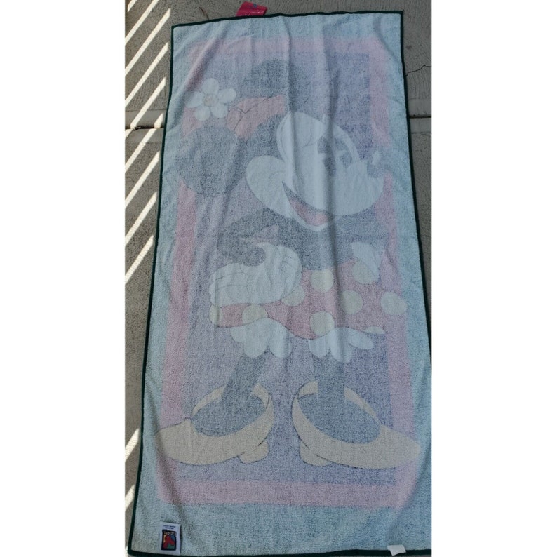 Pu&ograve; includere: Un asciugamano da spiaggia bianco con un'immagine colorata di Minnie Mouse che indossa un vestito rosso a pois e un fiore giallo nei capelli.