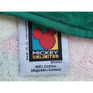 Pu&ograve; includere: Etichetta bianca con una testa di Topolino rossa e il testo "Mickey Unlimited" con un simbolo di copyright Disney. L'etichetta riporta anche "100% Cotone (Algod&oacute;n-Coton)" e "Made in El Salvador".